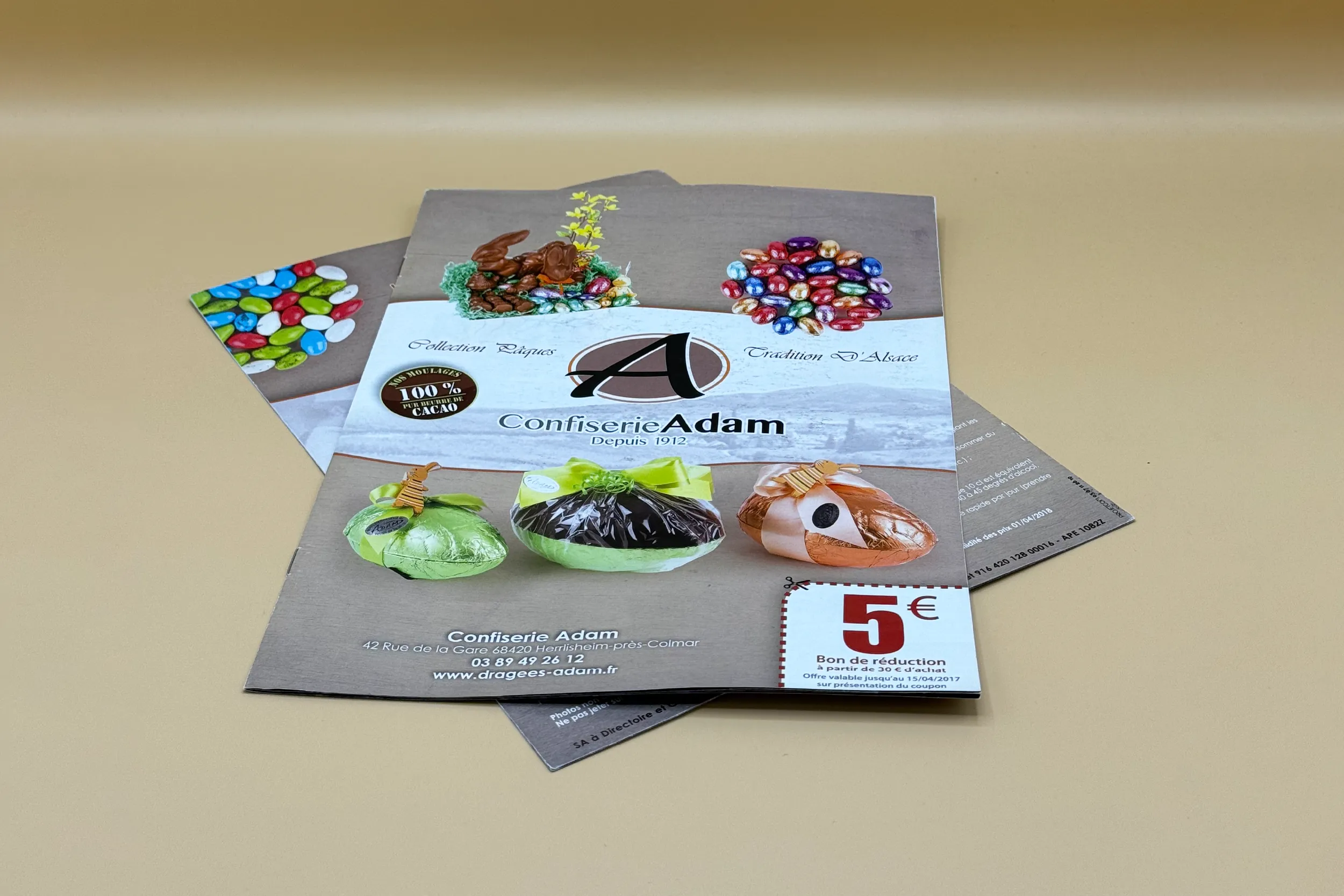 Catalogues produits de la Confiserie Adam fermés, sur un fond bois clair et naturel.