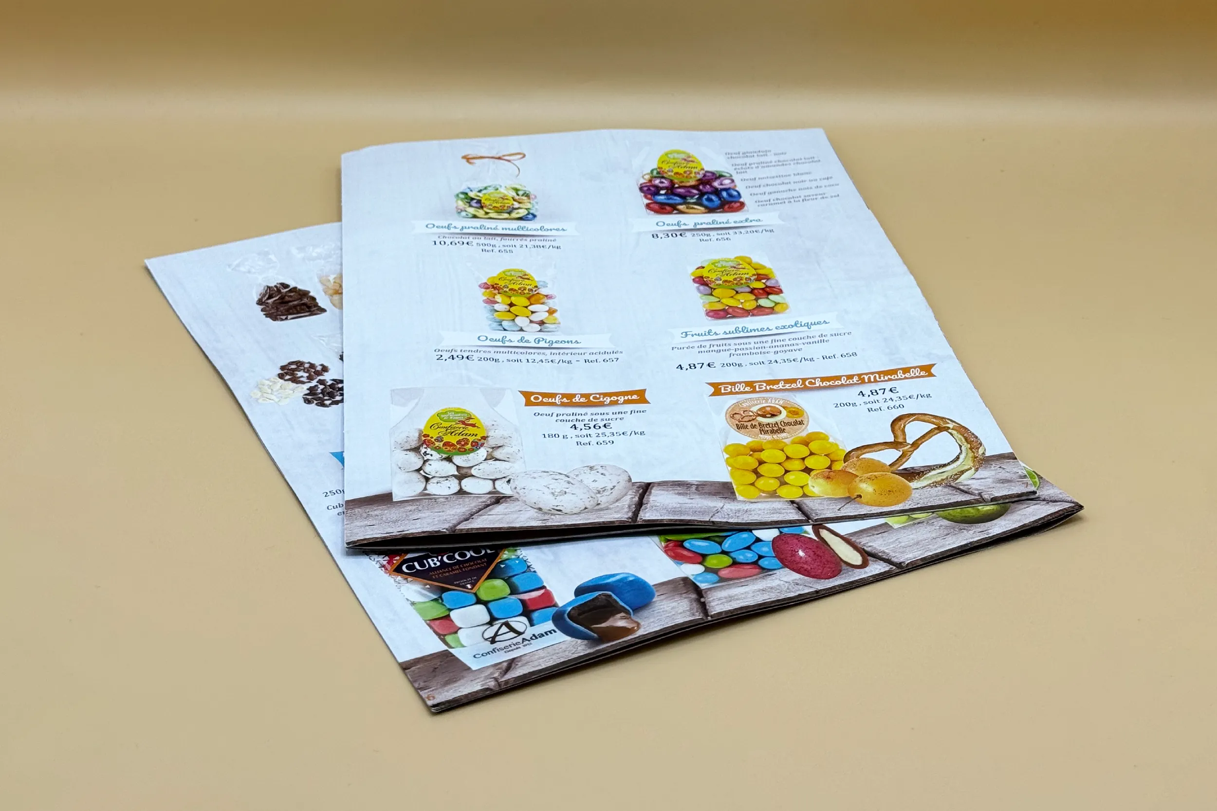 Catalogues produits de la Confiserie Adam ouverts, sur un fond bois clair et naturel.